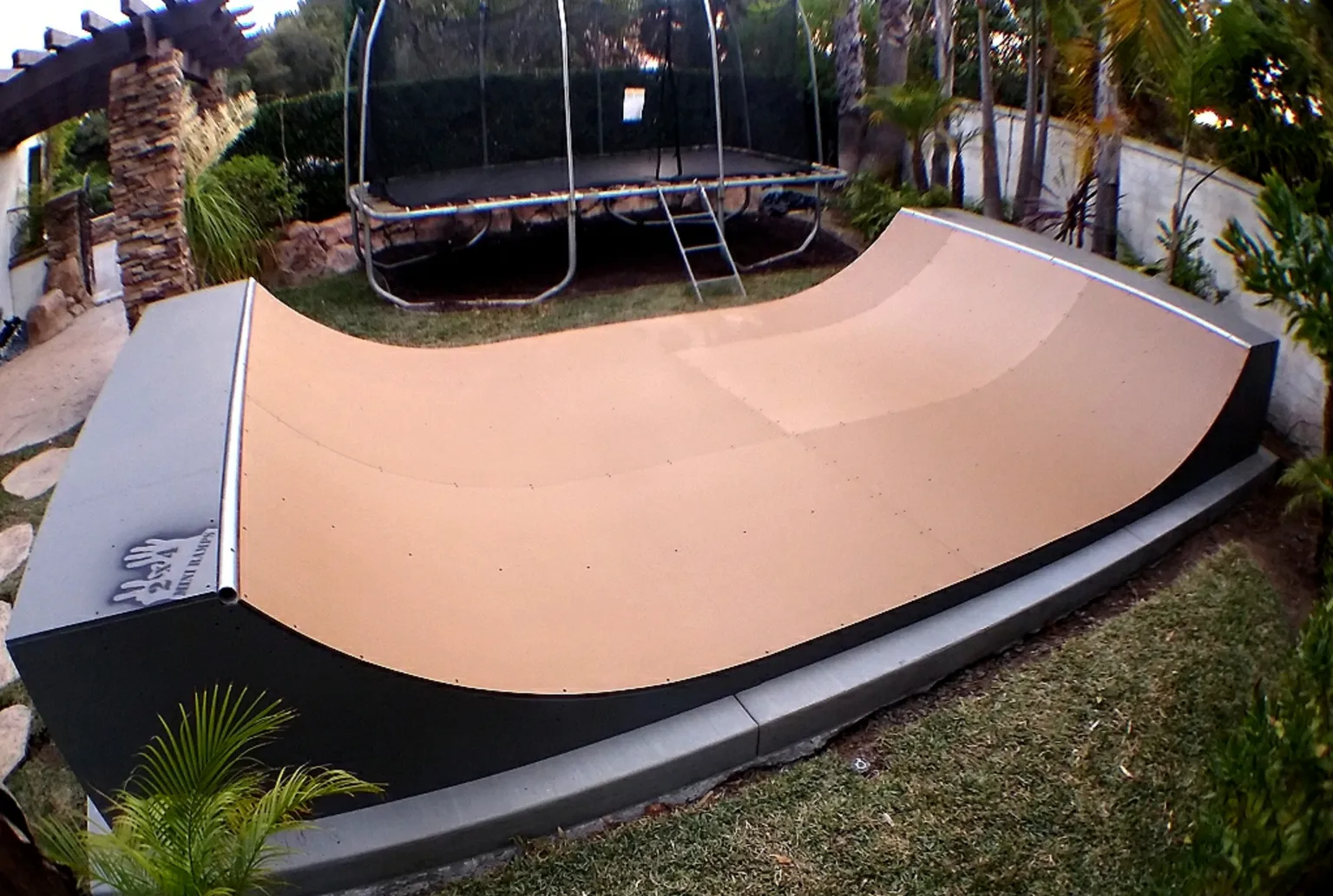 Two and a half foot high miniramp in backyard on foundation footer blocks with a trampoline in the background