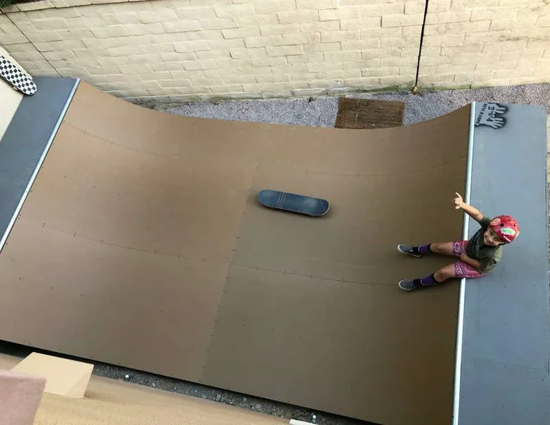 Top down view of miniramp with child sitting in the deck and board on the flat bottom for scale
