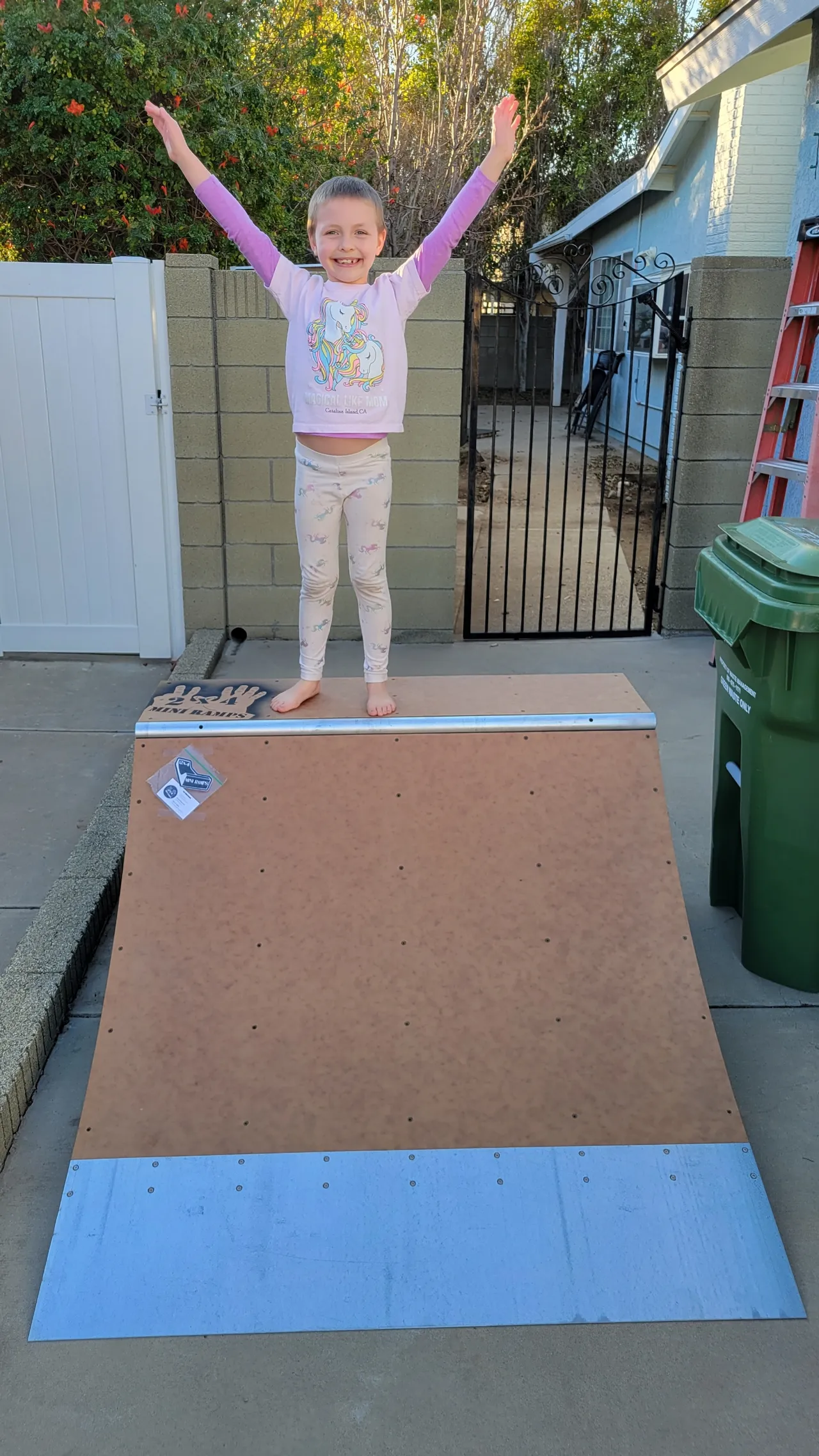 Child on deck of two foot high by four foot wide quarter pipe smiling with hands up in the air