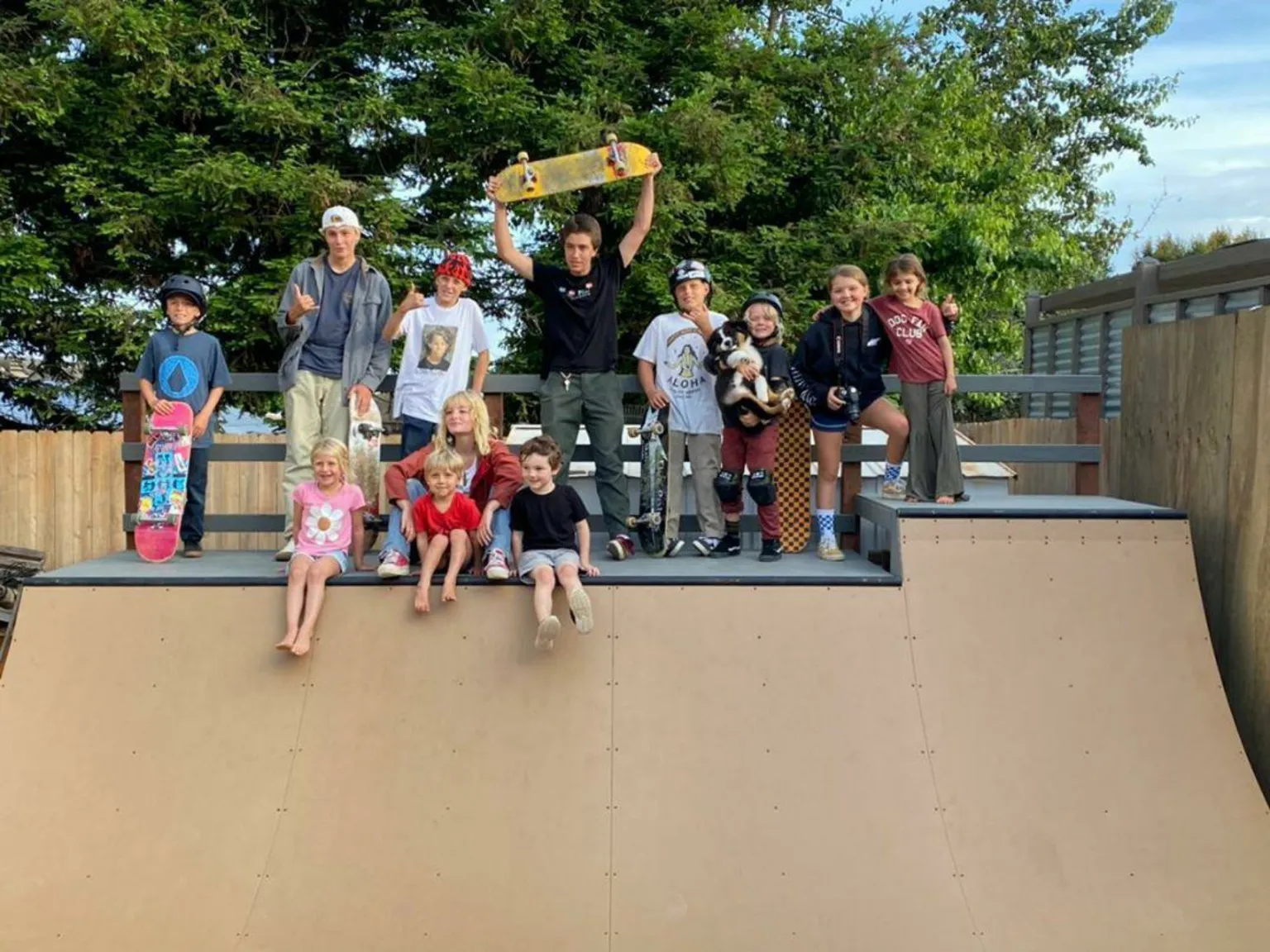 Lots of skaters standing on the deck of a four foot high miniramp smiling and posing
