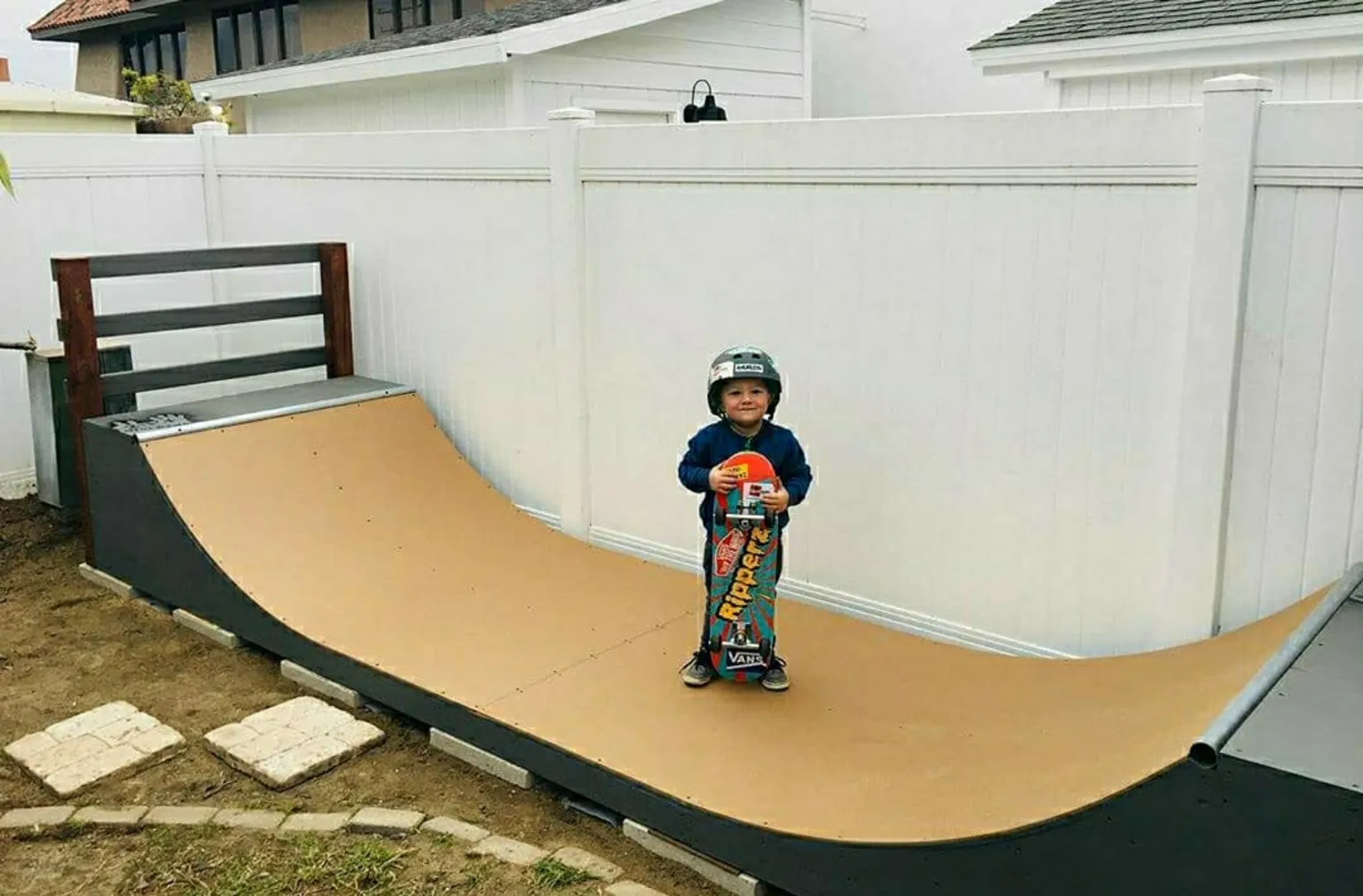 Original 2x4 miniramp with young kid standing in the middle with board, smiling