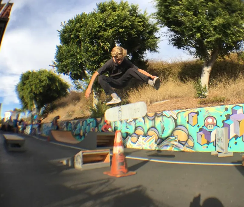 Child kickflipping over safety cone off 2x4 built launch ramp as other children watch
