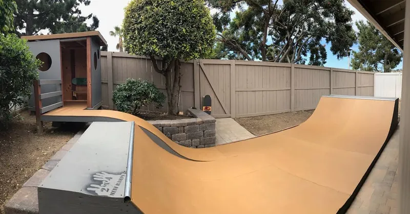 Side view of custom miniramp with roll-in and tree house style enclosure with bench made of skateboards